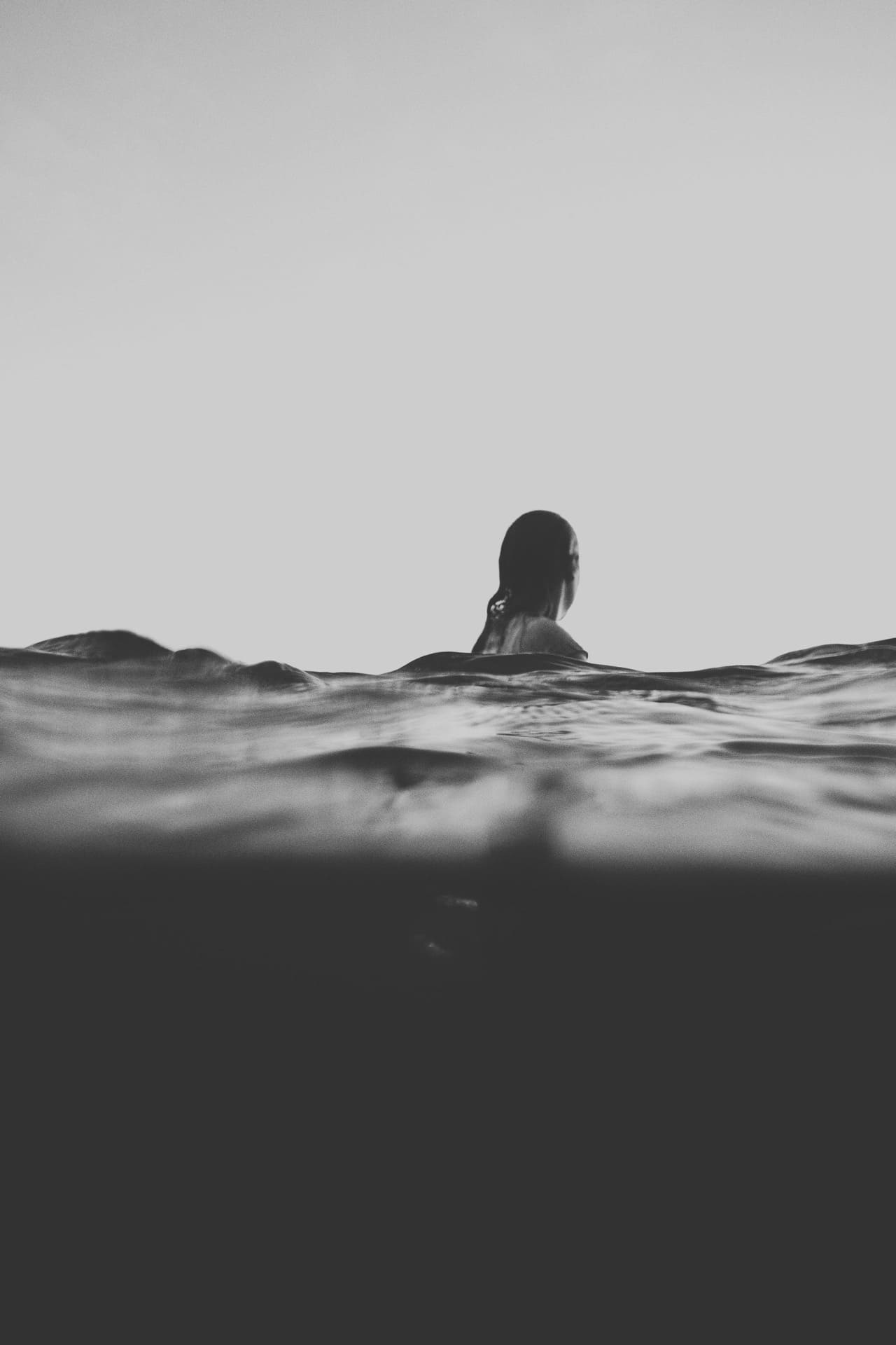 moody photograph bnw of girl swimming in sea with head above water
